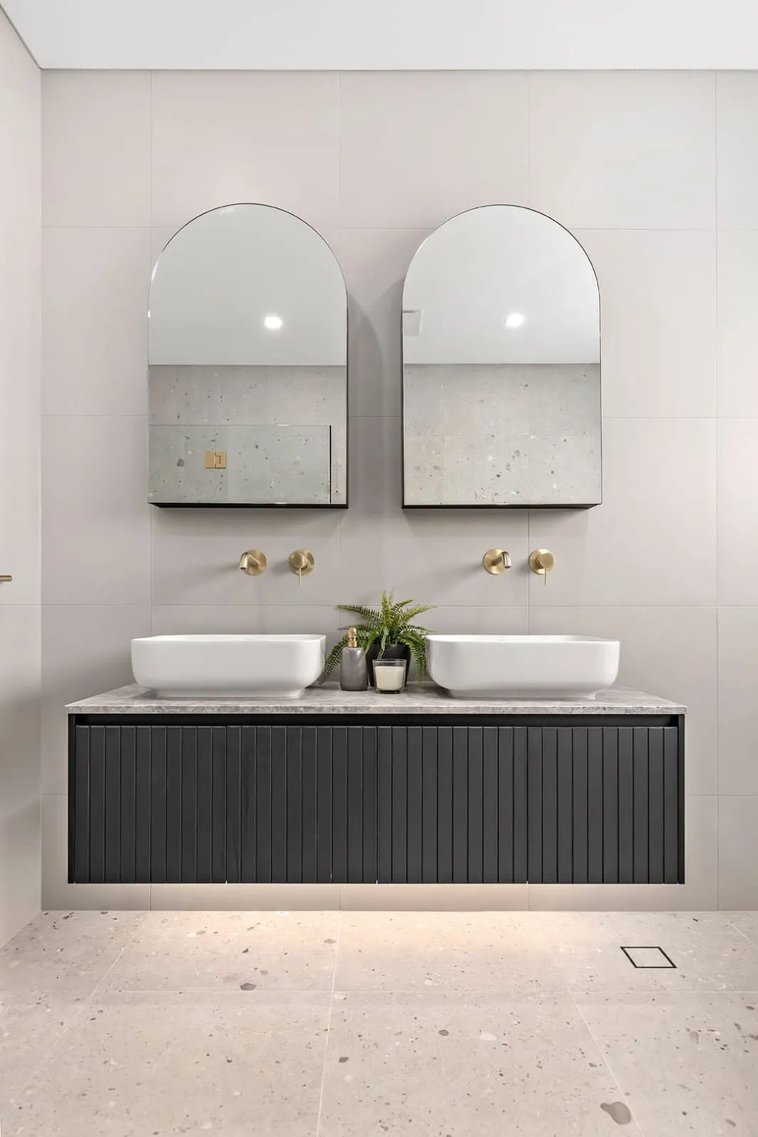 Double floating vanity with two arched mirrors and brass wall taps over a terrazzo floor