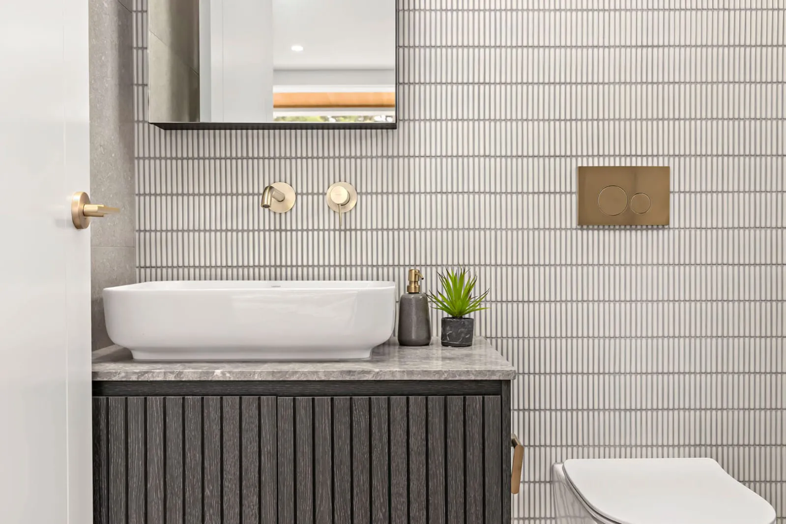 Vessel basin on a dark fluted vanity with vertical white wall tiles and brass taps
