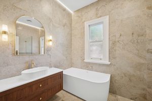 Federation bathroom renovation, Haberfield, after: travertine-look tiles, arched mirror, wall sconces and freestanding bath